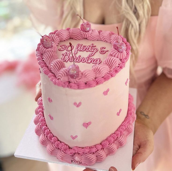 a woman holding up a pink and white cake with hearts on it's side