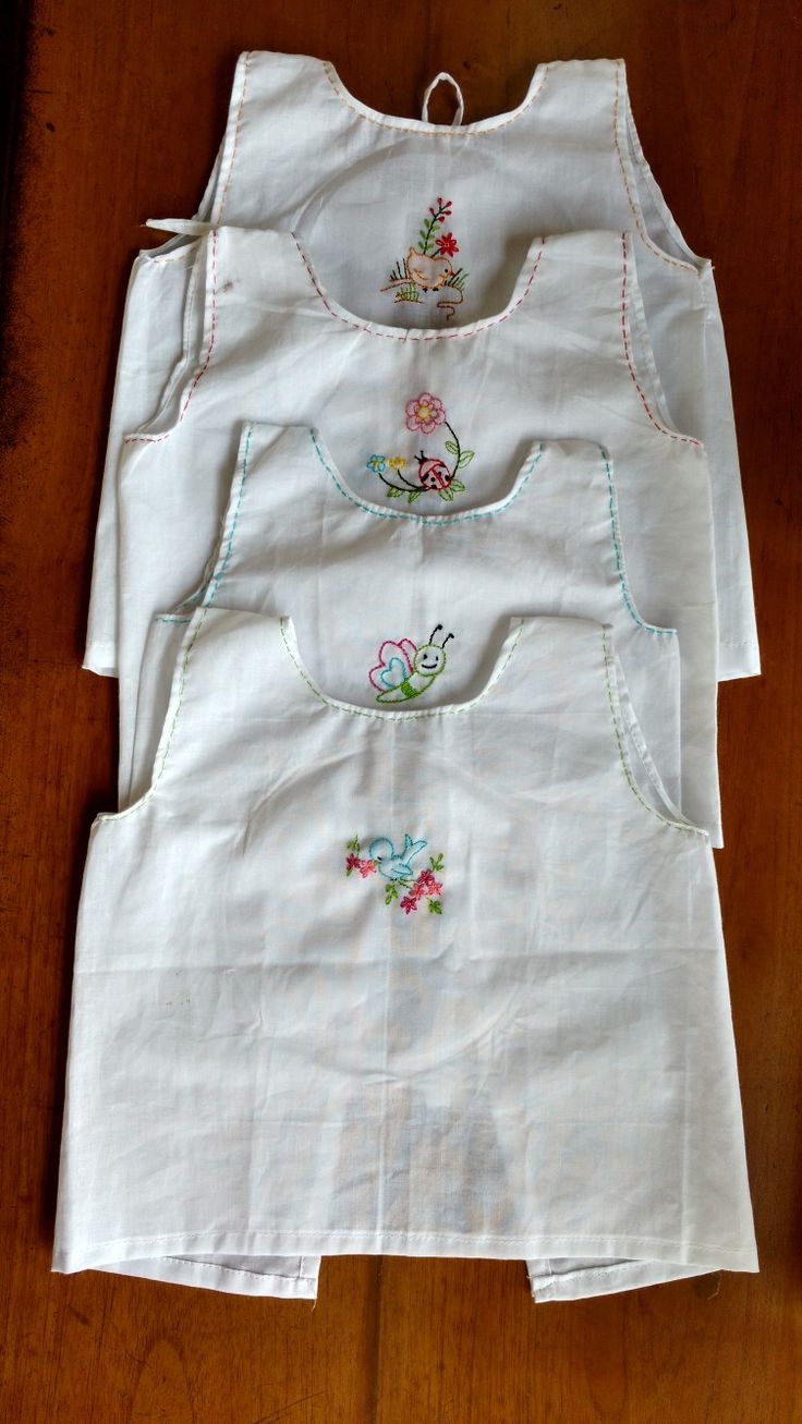 three white shirts with embroidered flowers on them sitting on a wooden floor next to a bottle