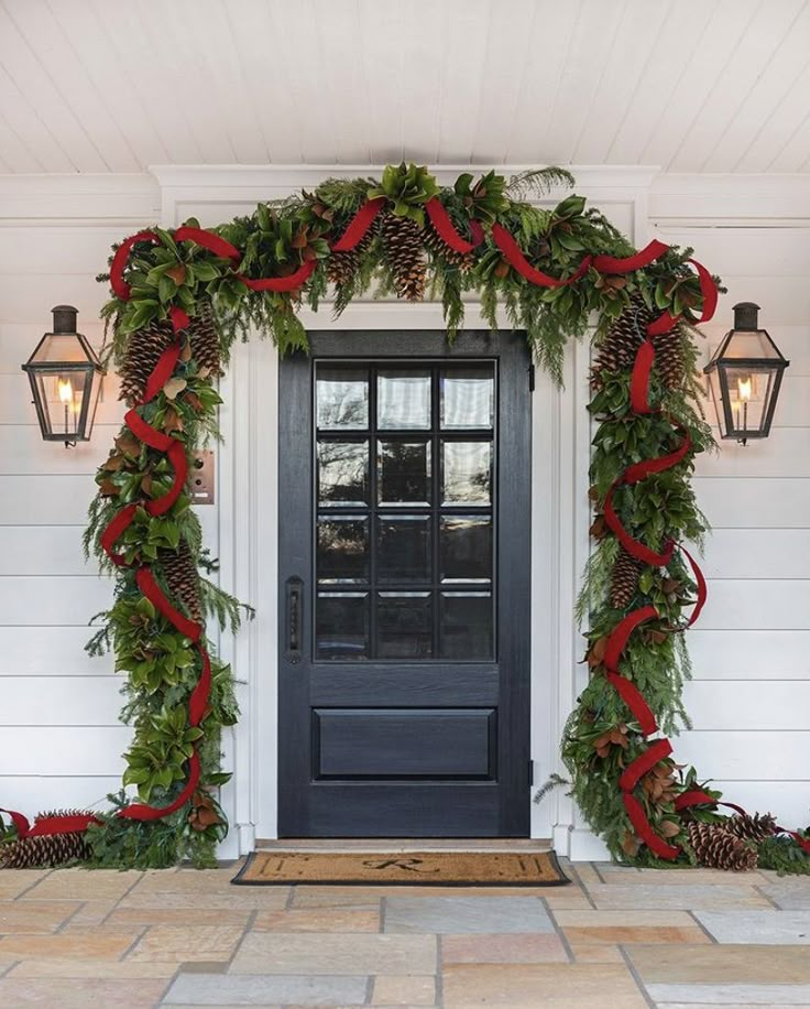 a black front door decorated with christmas greenery and pine cones, red ribbon and bows