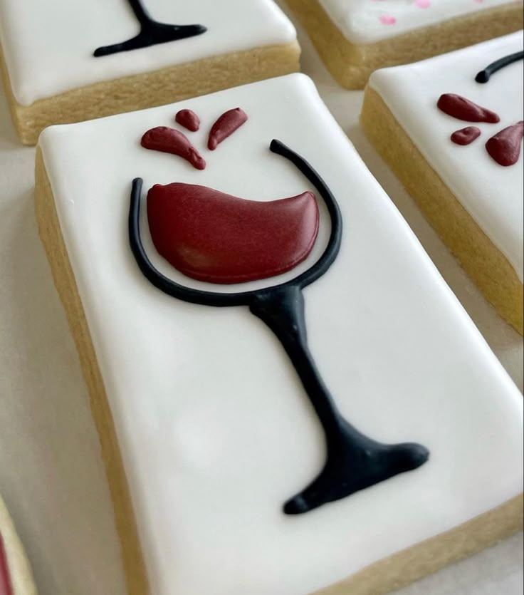 four decorated cookies with red and black icing sitting on top of each other in the shape of wine glasses