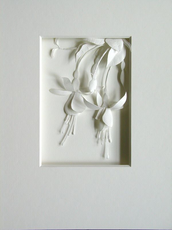 a white paper sculpture with flowers and leaves on it's side in a square frame