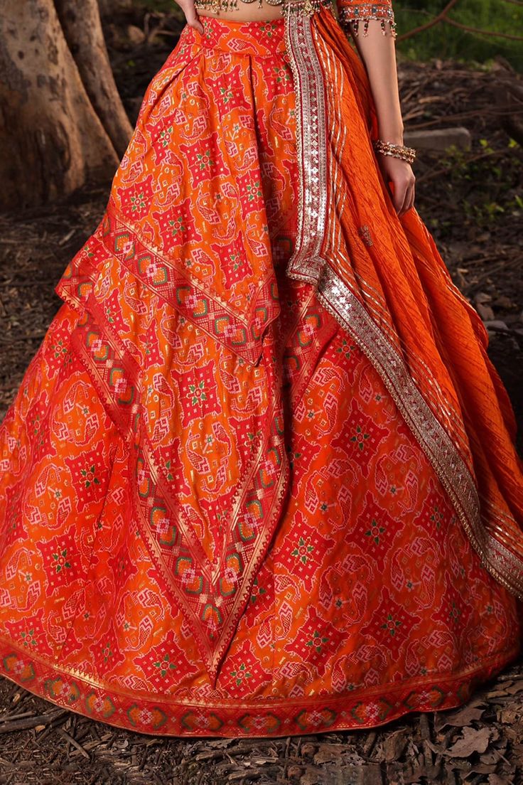 Carrot orange ikat weave lehenga with asymmetric layers. Paired with zardozi embroidered asymmetric blouse and fitted sleeves. Comes with hand crushed dupatta and Meenakari embellished belt.
Components:4
Pattern:Embroidered
Type of Work:Zardozi and Mirror Work
Neckline:Scoop
Sleeve Length:Straight Three Quarter
Fabric:Lehenga: Banarasi Silk; Blouse: Pure Silk; Dupatta: Shimmer Organza
Color:Orange
Other Details:
Bead hem blouse
Layered lehenga
Tassel details
Note: The sleeveless blouse worn by t Orange Anarkali With Bandhani Print, Traditional Orange Sharara With Bandhani Print, Traditional Orange Bandhani Print Sharara, Orange Bandhani Print Dupatta For Wedding, Orange Bandhani Print Wedding Dupatta, Orange Lehenga For Festivals, Traditional Orange Bandhani Print Choli, Ceremonial Sharara With Tilla In Traditional Drape, Bollywood Style Orange Lehenga With Bandhani Print