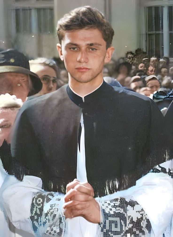 a man wearing a black shirt and white tie standing in front of a group of people