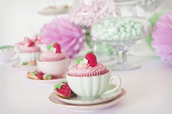 there are cupcakes with strawberries on top of them and pink flowers in the background