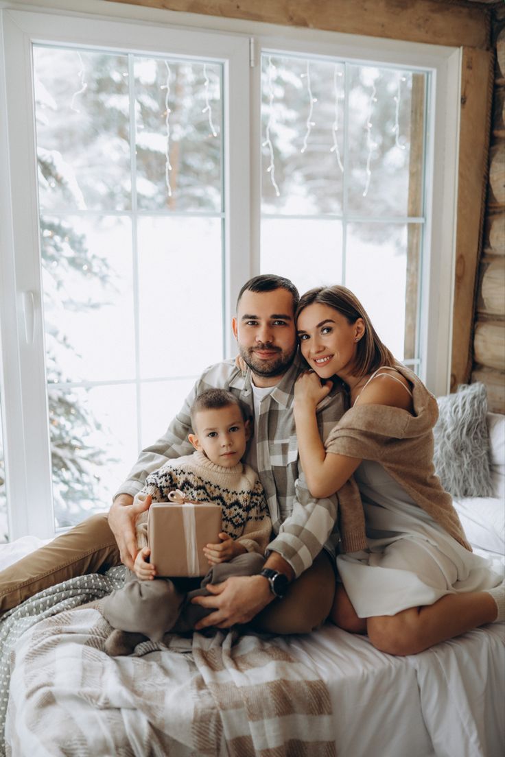 a man and woman sitting on a bed with a small child holding a present box