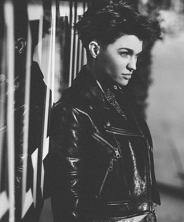 a black and white photo of a woman in a leather jacket leaning against a wall