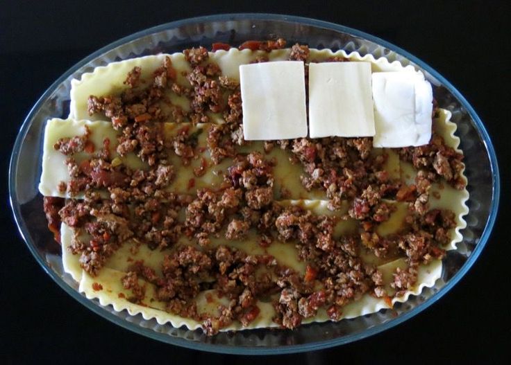 an uncooked dish with cheese and meat in it on a black table top