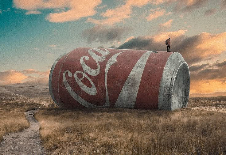 a man standing on top of a large coca - cola can in the middle of a field