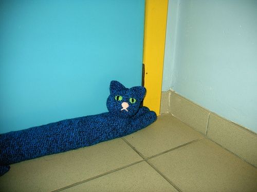 a blue knitted cat laying on the floor next to a yellow and blue wall