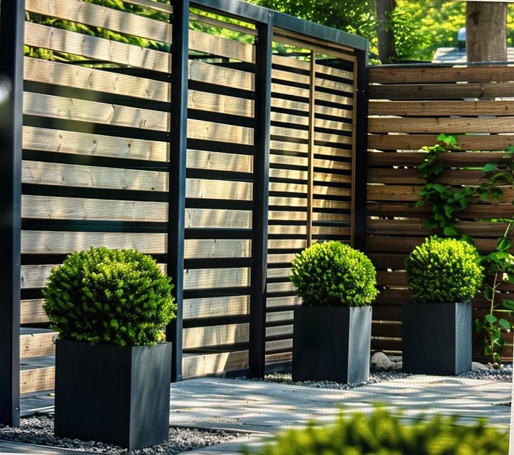 three black planters are in front of a wooden fence and some bushes on the ground