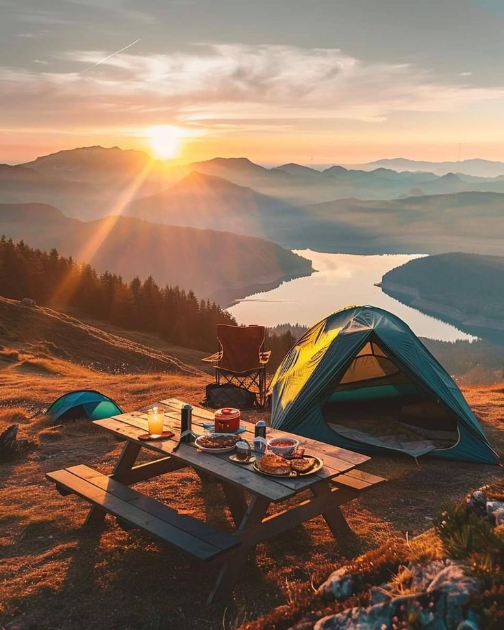 a tent set up on top of a mountain with the sun setting in the background