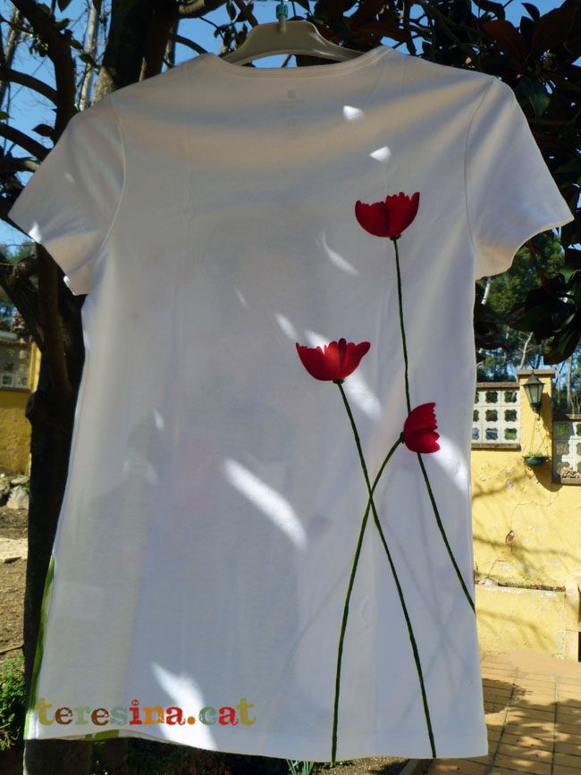 a t - shirt with three red flowers painted on it hanging from a tree branch