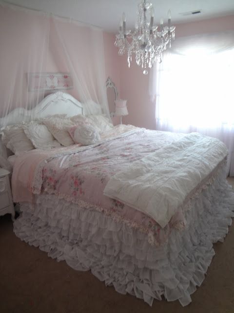 a white bed sitting in a bedroom next to a window with a chandelier