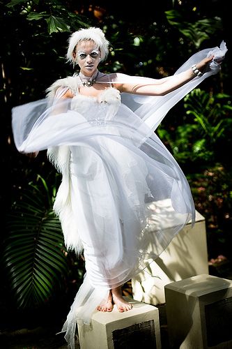 a woman with white hair and makeup is dressed in an angel costume, standing on two blocks