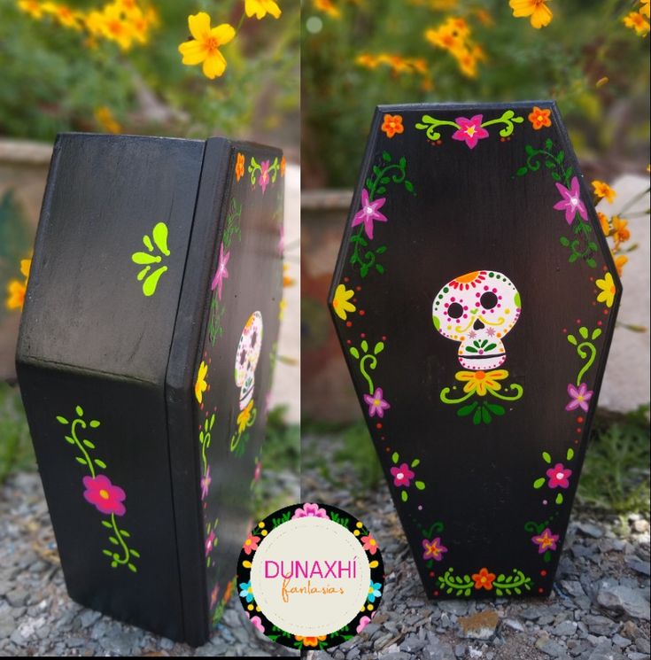 two black boxes with flowers painted on them and one has a skull in the middle