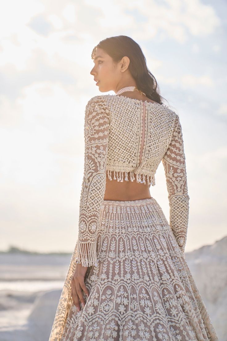 a woman in a white dress standing on the beach with her back to the camera