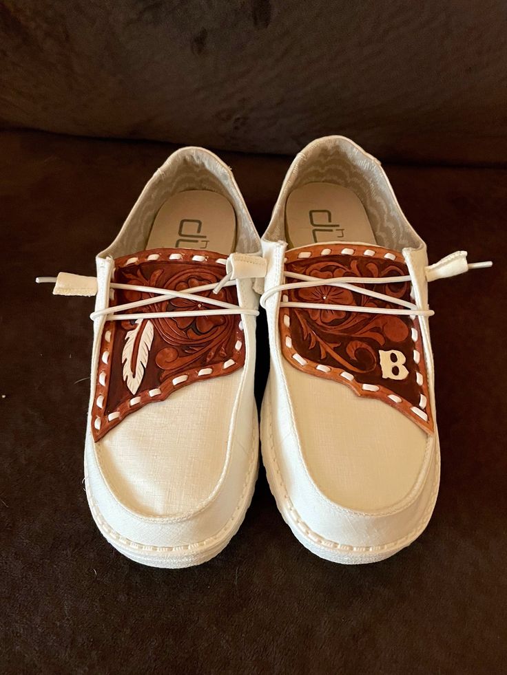 a pair of white shoes with brown leather bows on the top and bottom laces