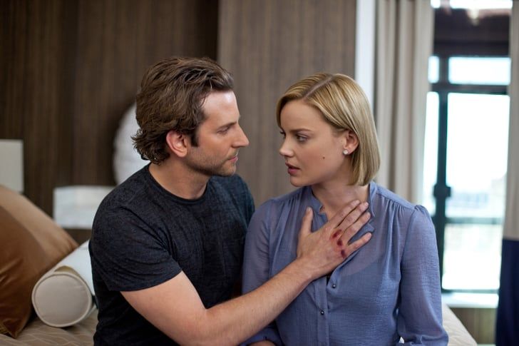 a man and woman sitting on top of a bed looking into each other's eyes