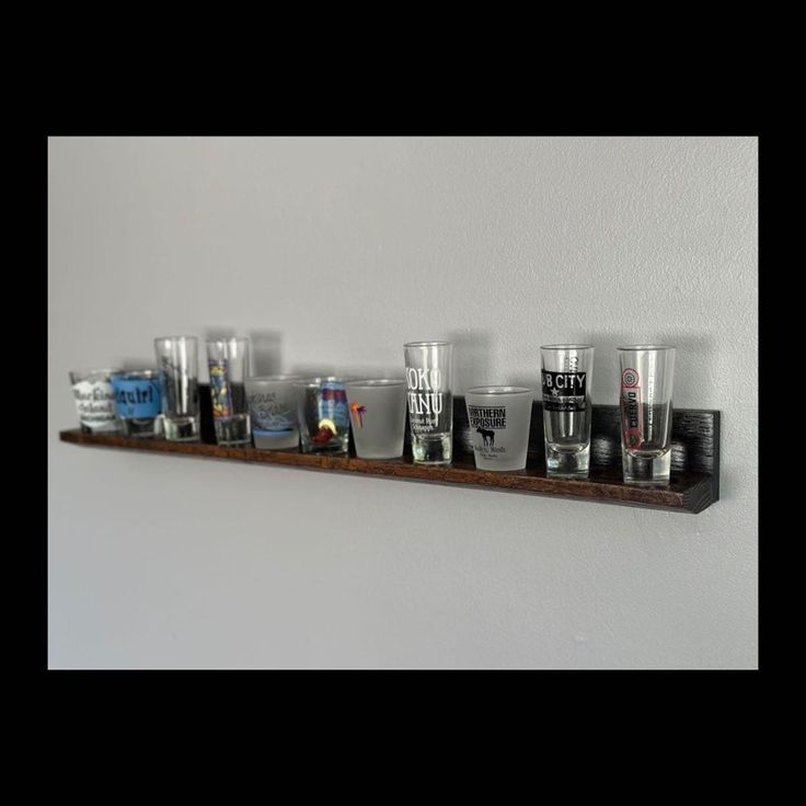 a row of shot glasses sitting on top of a wooden shelf next to a wall