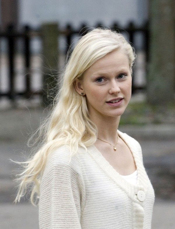 a woman with long blonde hair standing in front of a black fence and looking at the camera