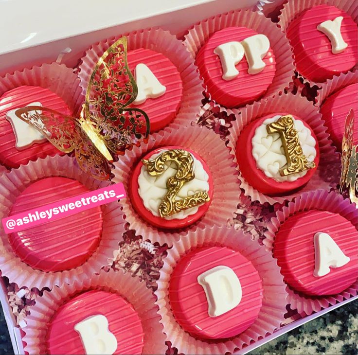 pink cupcakes decorated with gold and white icing are displayed in a box