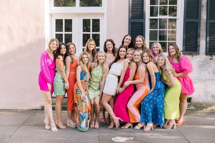 a group of women standing next to each other in front of a pink building with shutters