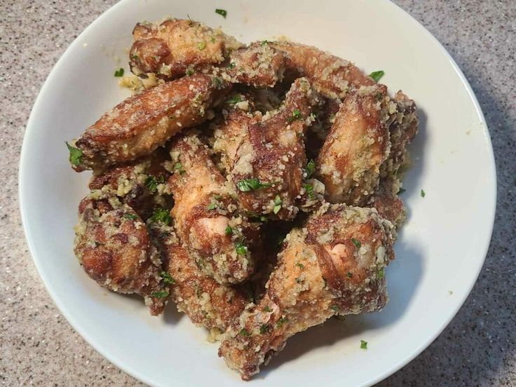 a white plate topped with fried chicken wings covered in parsley on top of a table