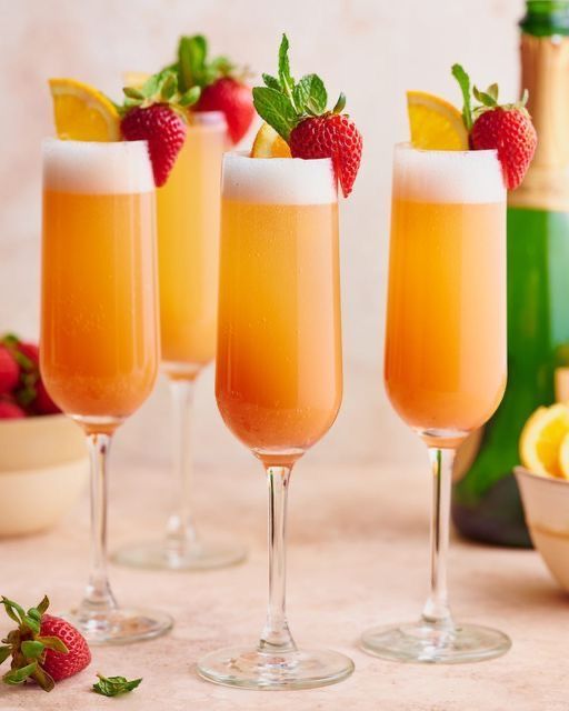 three glasses filled with champagne and strawberries on top of a table next to fruit