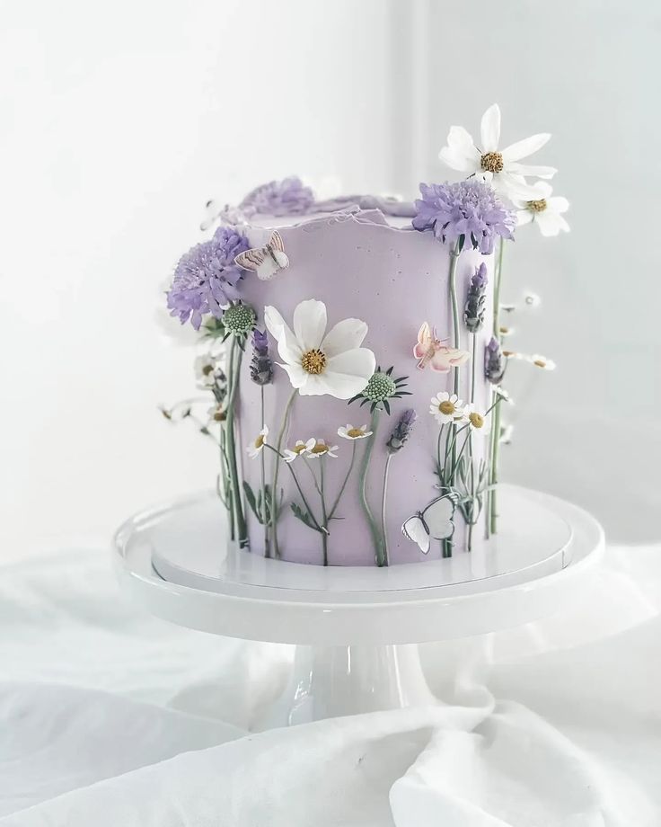 a purple cake with white flowers on it sitting on top of a table next to a white sheet