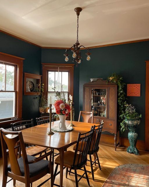 a dinning room table and chairs in front of two windows with potted plants on them