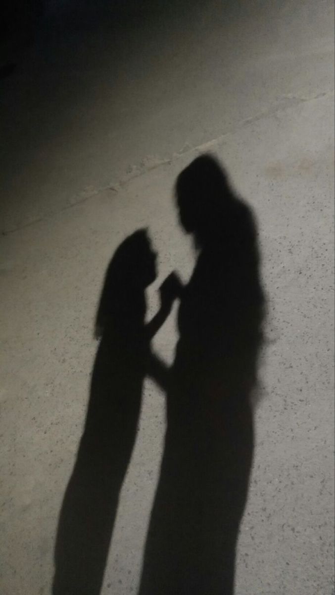 two people standing next to each other in the dark with their shadow on the ground