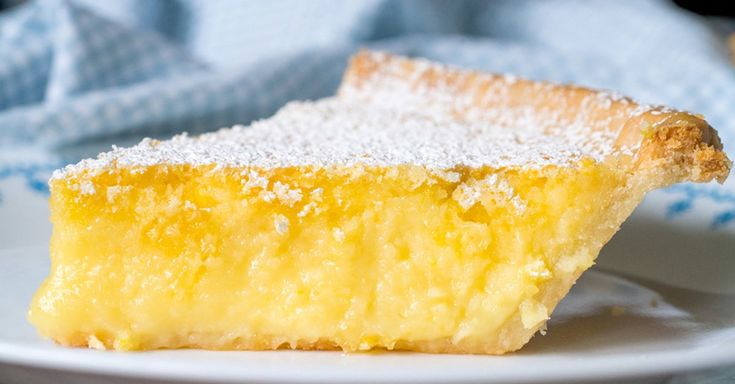 a slice of lemon pie on a plate with powdered sugar over it and a blue towel in the background