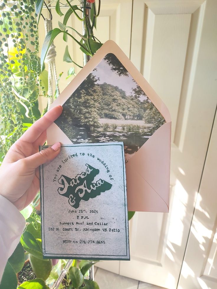 a person holding up an old postcard in front of a house with a pond