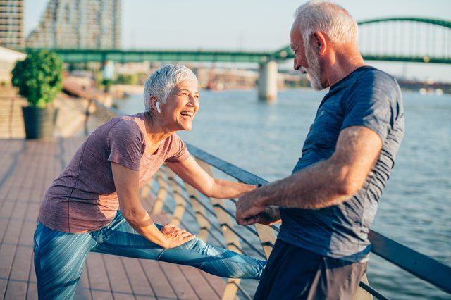 an older man and woman doing stretching exercises on a bridge near the water with a city in the background