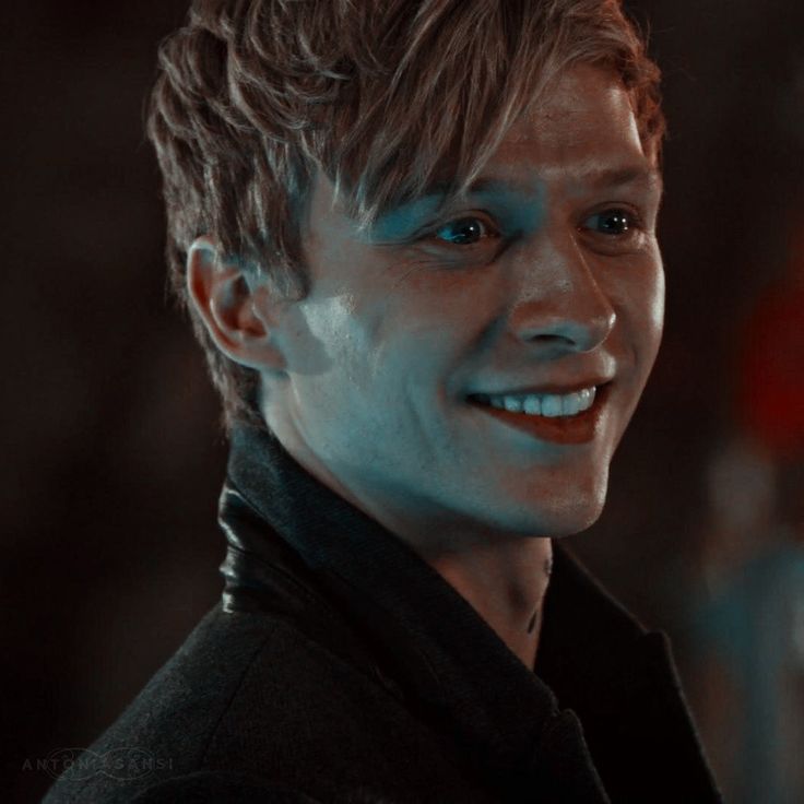 a close up of a person wearing a black jacket and smiling at the camera with blue eyes