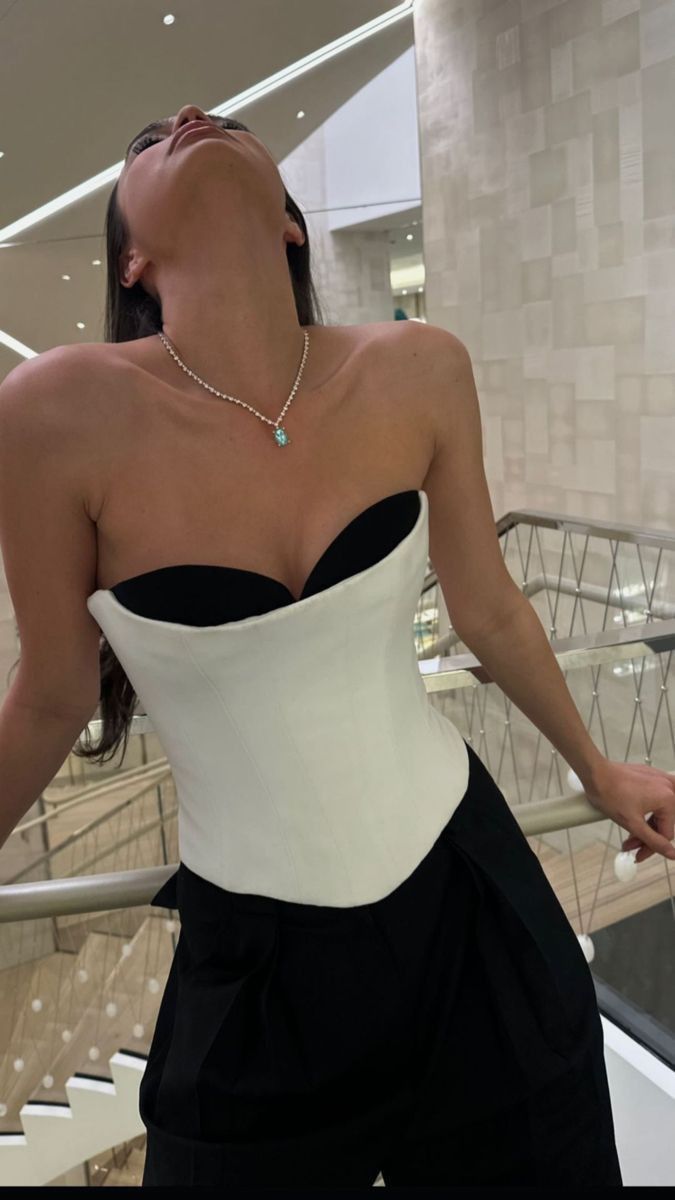 a woman in a white and black corset is standing on the stairs with her eyes closed