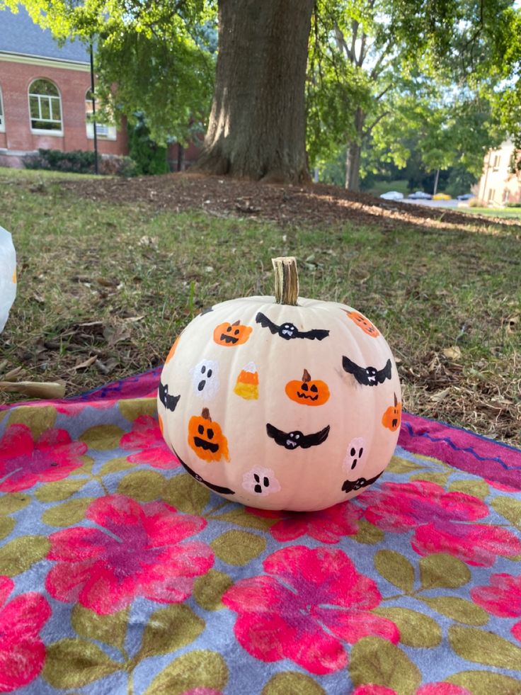 a painted pumpkin sitting on top of a colorful blanket in front of a large tree