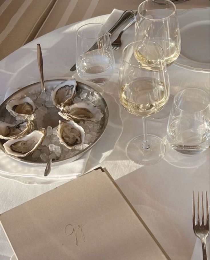 an empty plate with oysters on it next to wine glasses and utensils