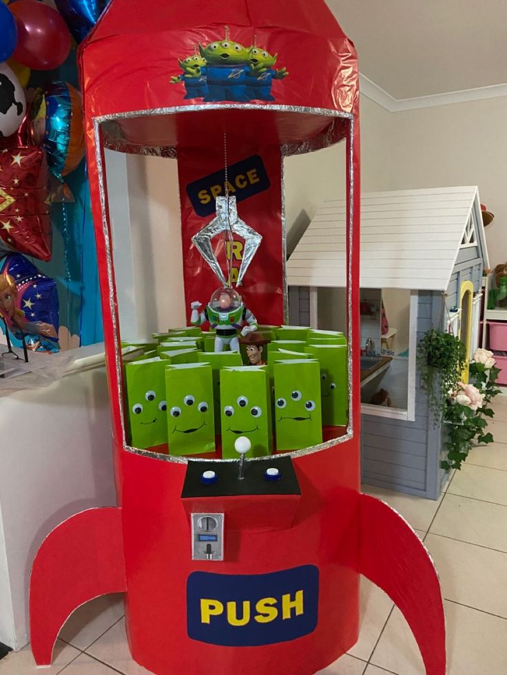 a red and green machine sitting on top of a tiled floor next to balloons in the background