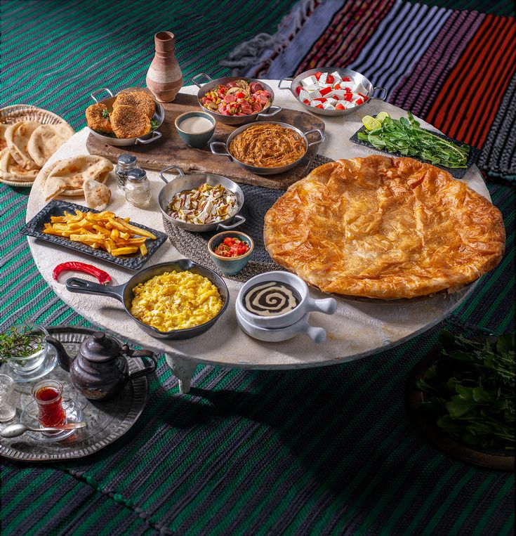 a table topped with lots of food on top of a green rug next to plates and bowls