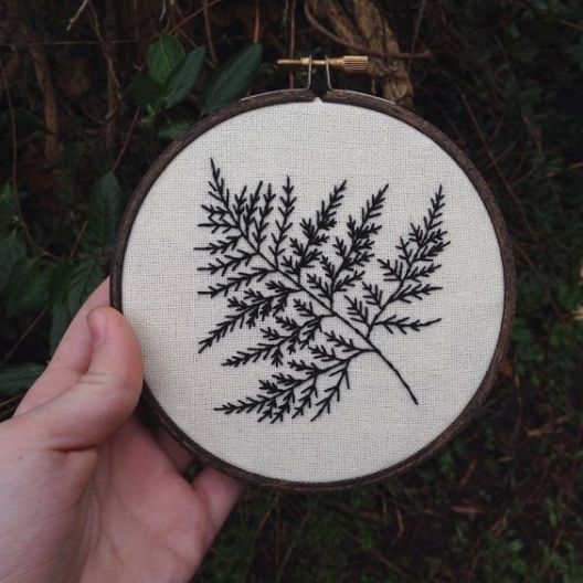 a hand is holding up a cross - stitched embroidery piece with black and white leaves on it