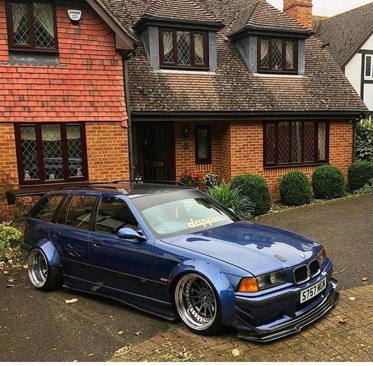 a blue bmw is parked in front of a large brick house with two story windows