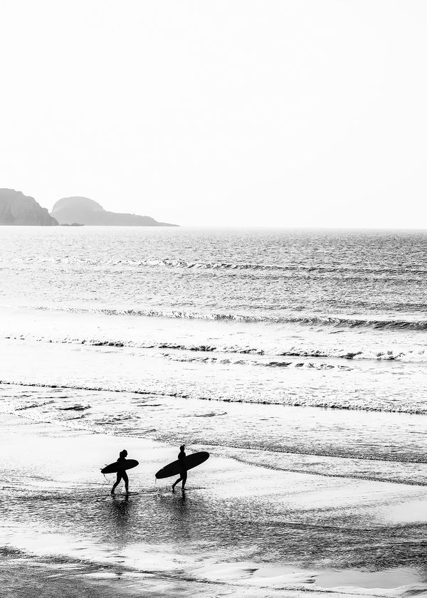 two people carrying surfboards walking into the ocean