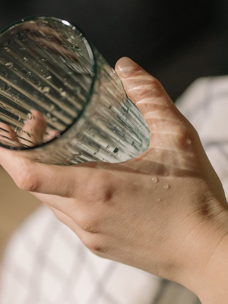 a person holding a glass in their hand with water coming out of the top and bottom