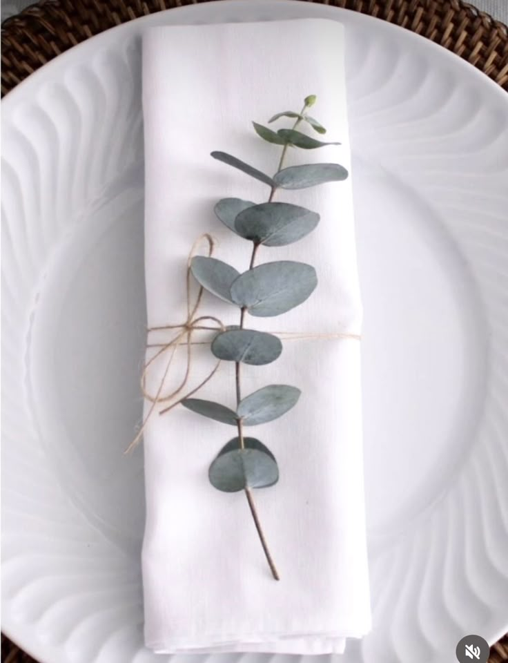 a white plate topped with a napkin covered in eucalyptus leaves