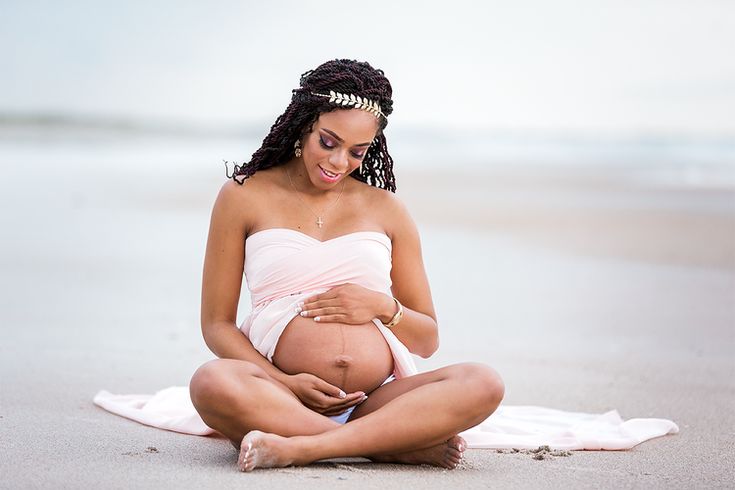 a pregnant woman is sitting on the beach