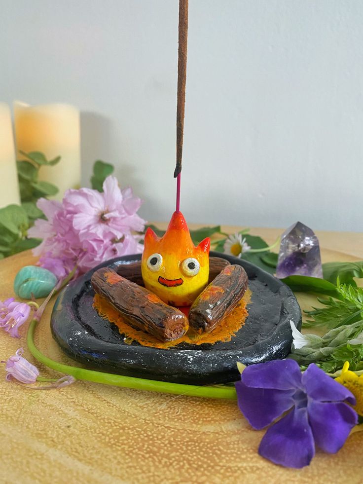 a small yellow fish sitting on top of a black plate next to flowers and candles