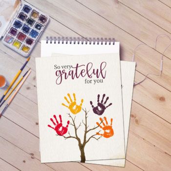 a notepad with hand prints on it next to paintbrushes and watercolors