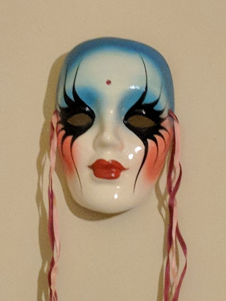 a white mask with blue and red makeup on it's face is hanging from a wall