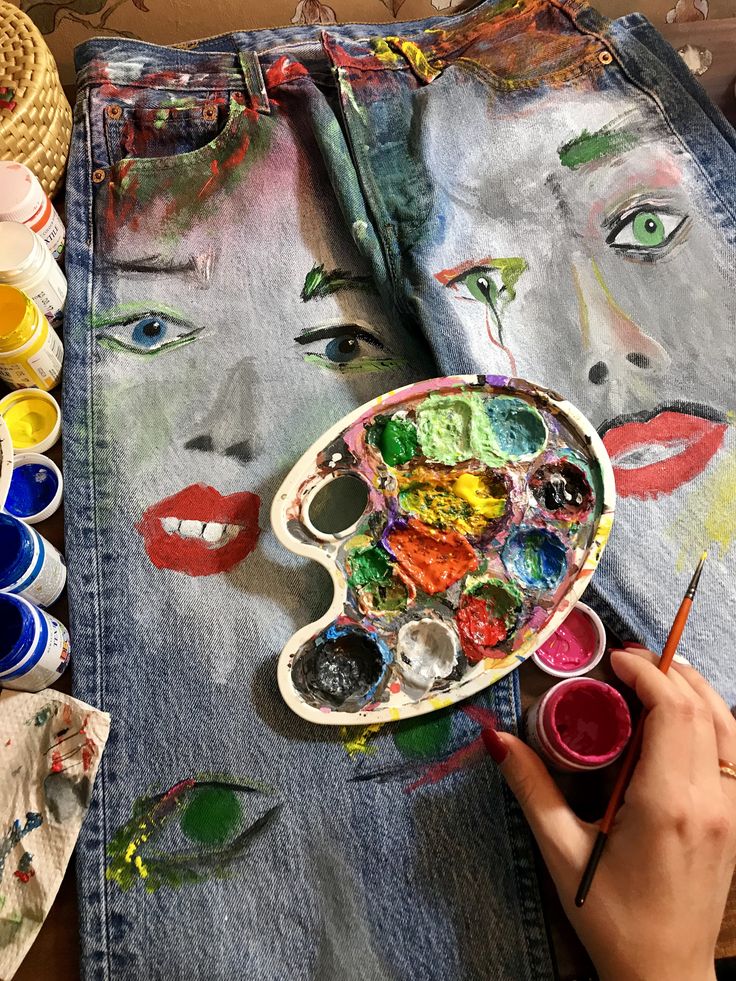 a person painting on a jean jacket with colorful paints and brushes in front of them